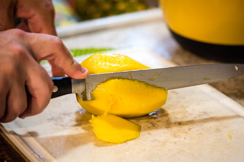 slicing mango with knife on white cutting board