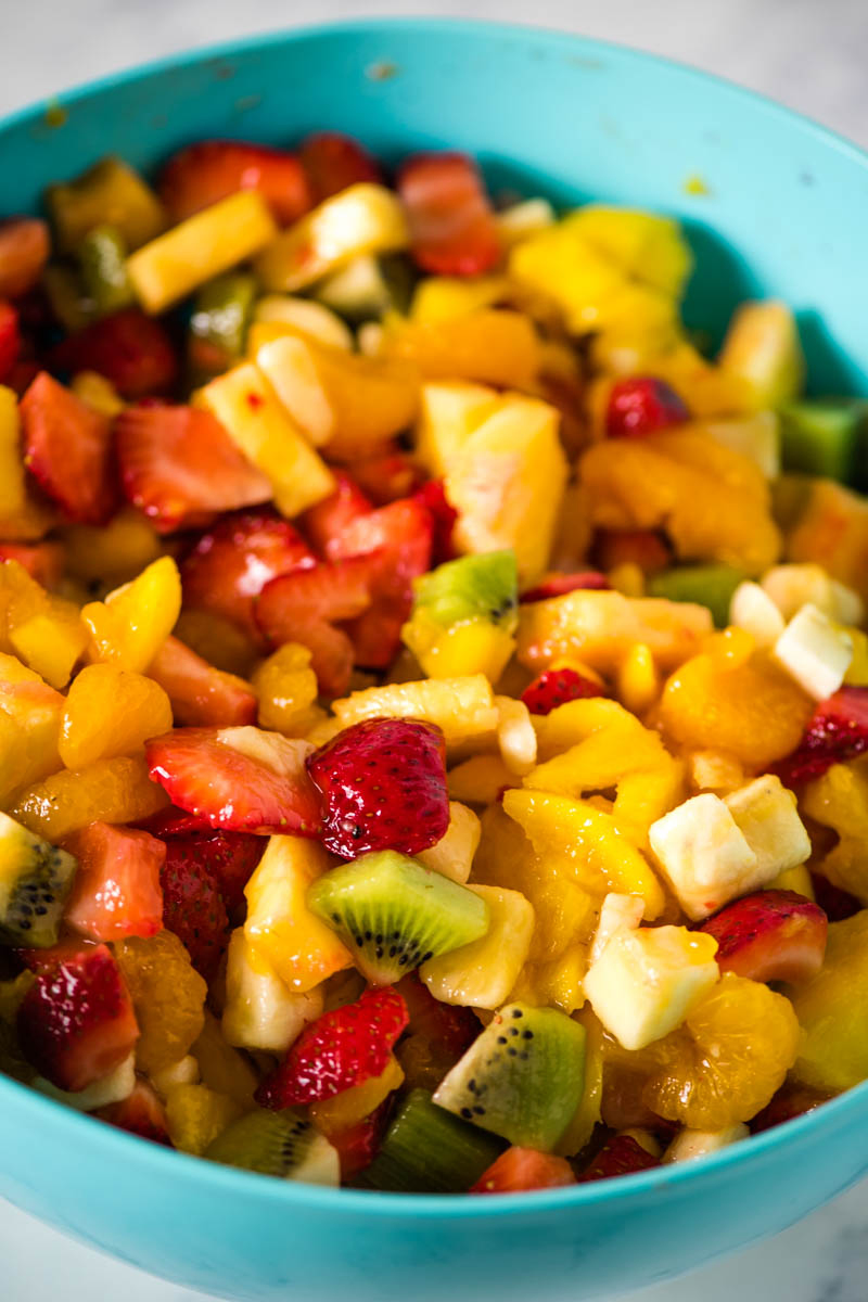freshly-mixed tropical fruit salad mixture in a large blue mixing bowl on a marbled white countertop