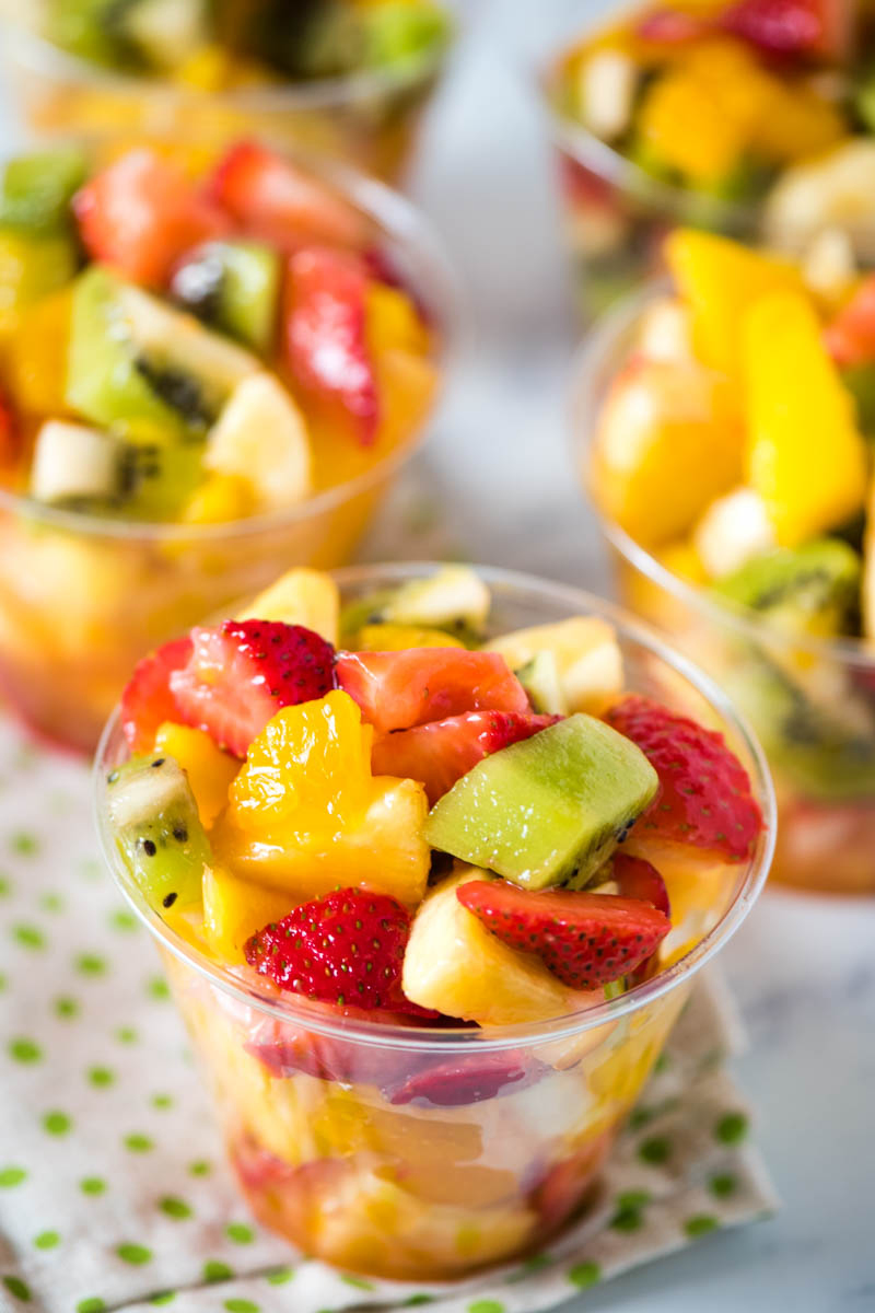 tropical homemade fruit salad cups in small disposable plastic cups on green polka dot linen on white marble countertop