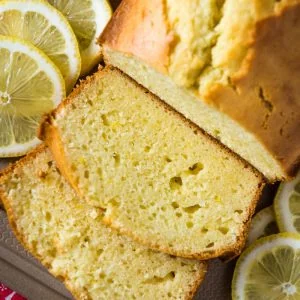 gluten free lemon loaf pound sliced up on a large gray cutting board with fresh lemon slices