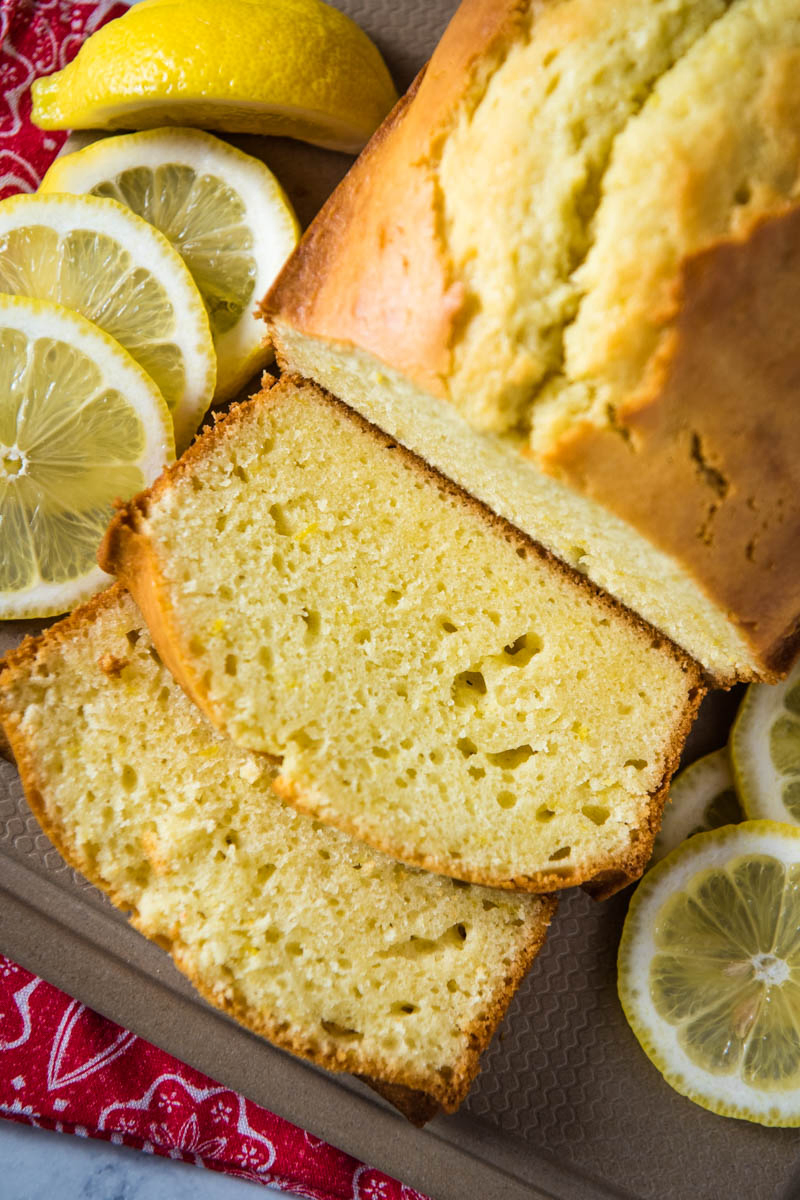 sliced loaf of gluten-free lemon pound cake on brown cutting board with lemon slices