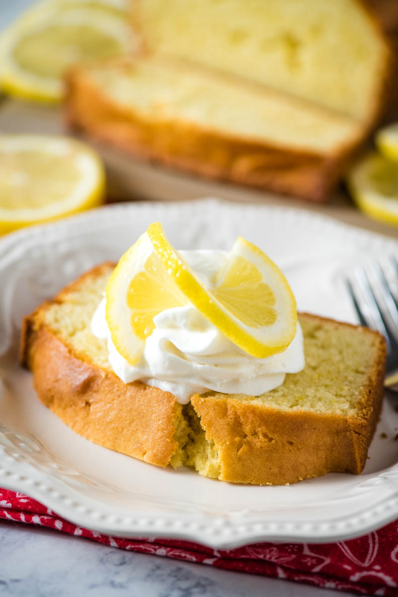 lemon slice and whipped cream on slice of GF lemon pound cake on white plate with fork