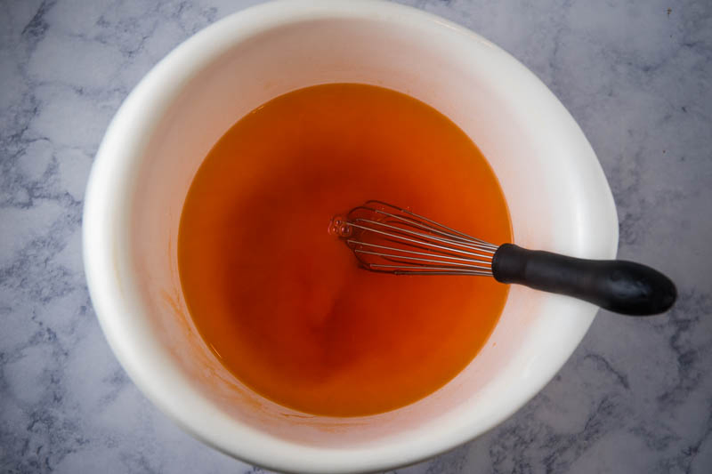 whisk and orange Jello mixture with boiling water in white mixing bowl