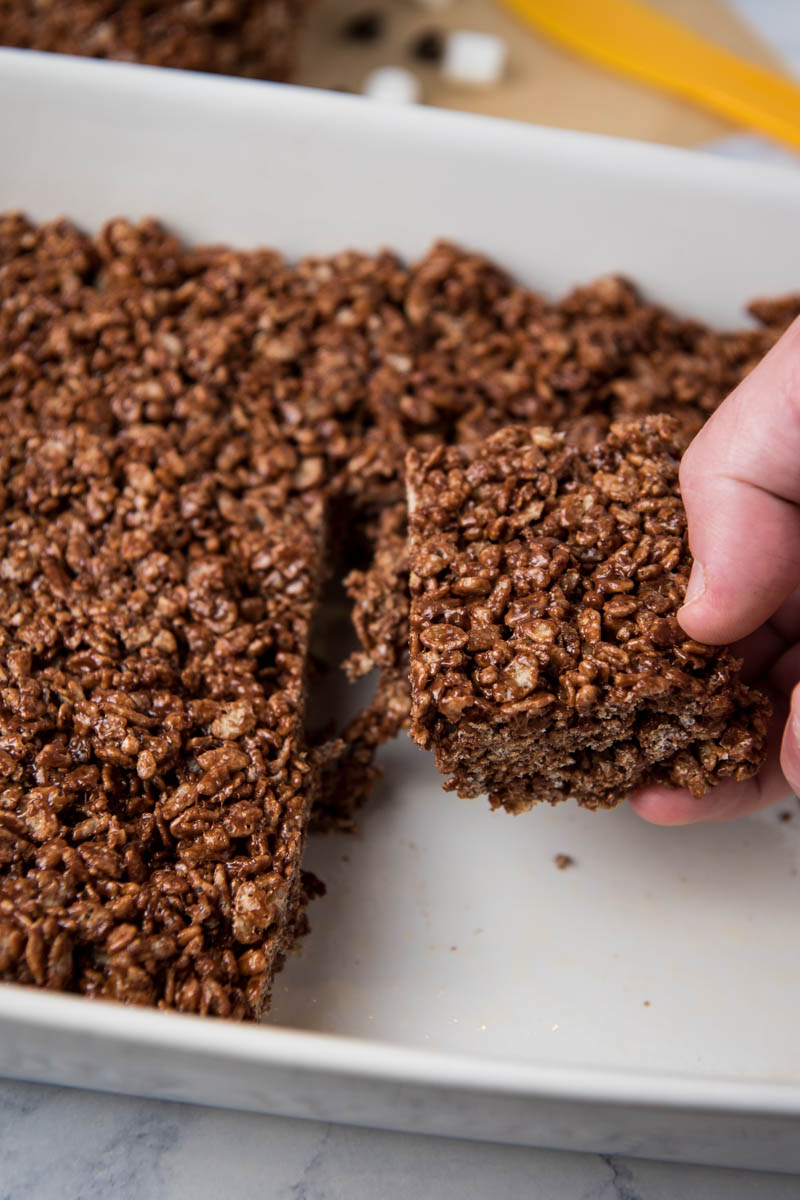 hand pulling no bake chocolate Rice Krispie squares from white baking dish