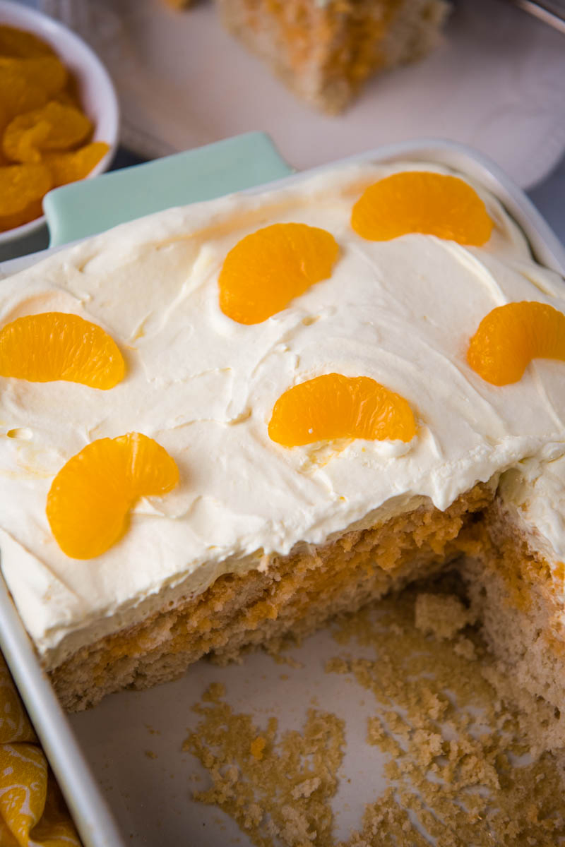 sliced orange Jello poke cake, topped with mandarin orange slices, in mint green and white baking dish