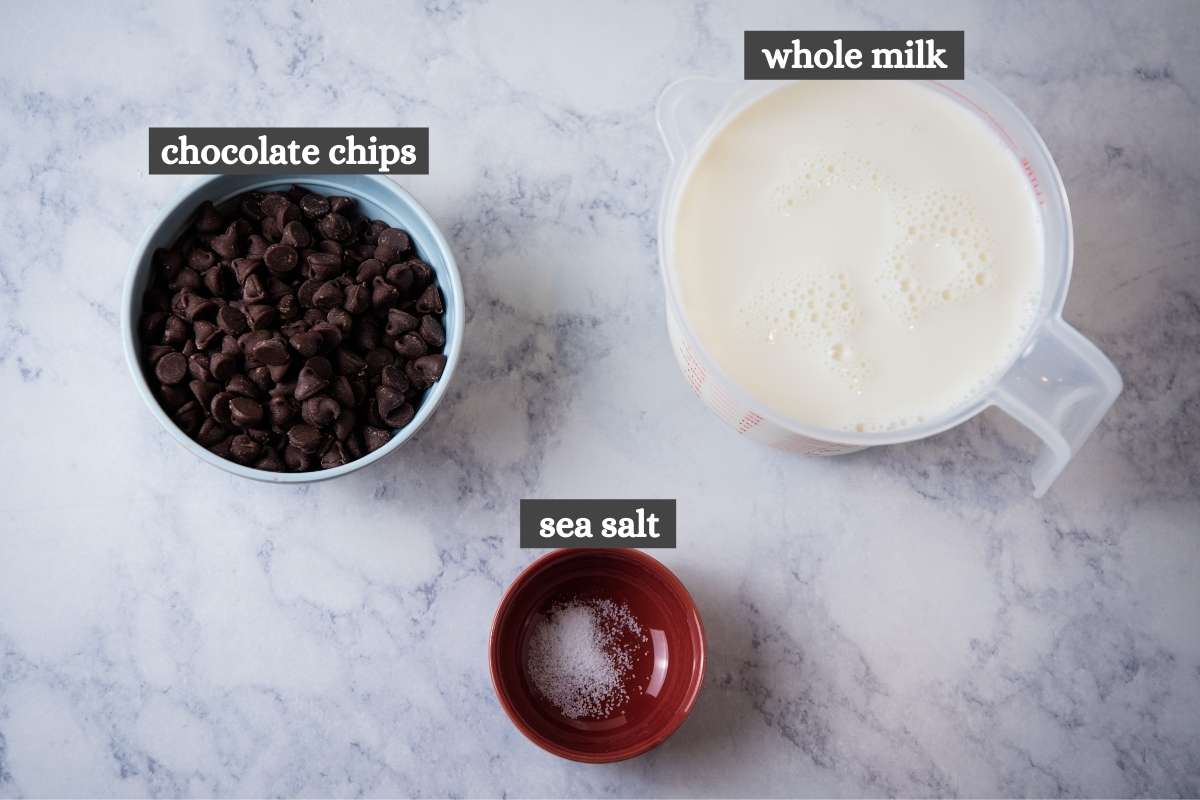 hot chocolate with chocolate chips ingredients on white marble countertop