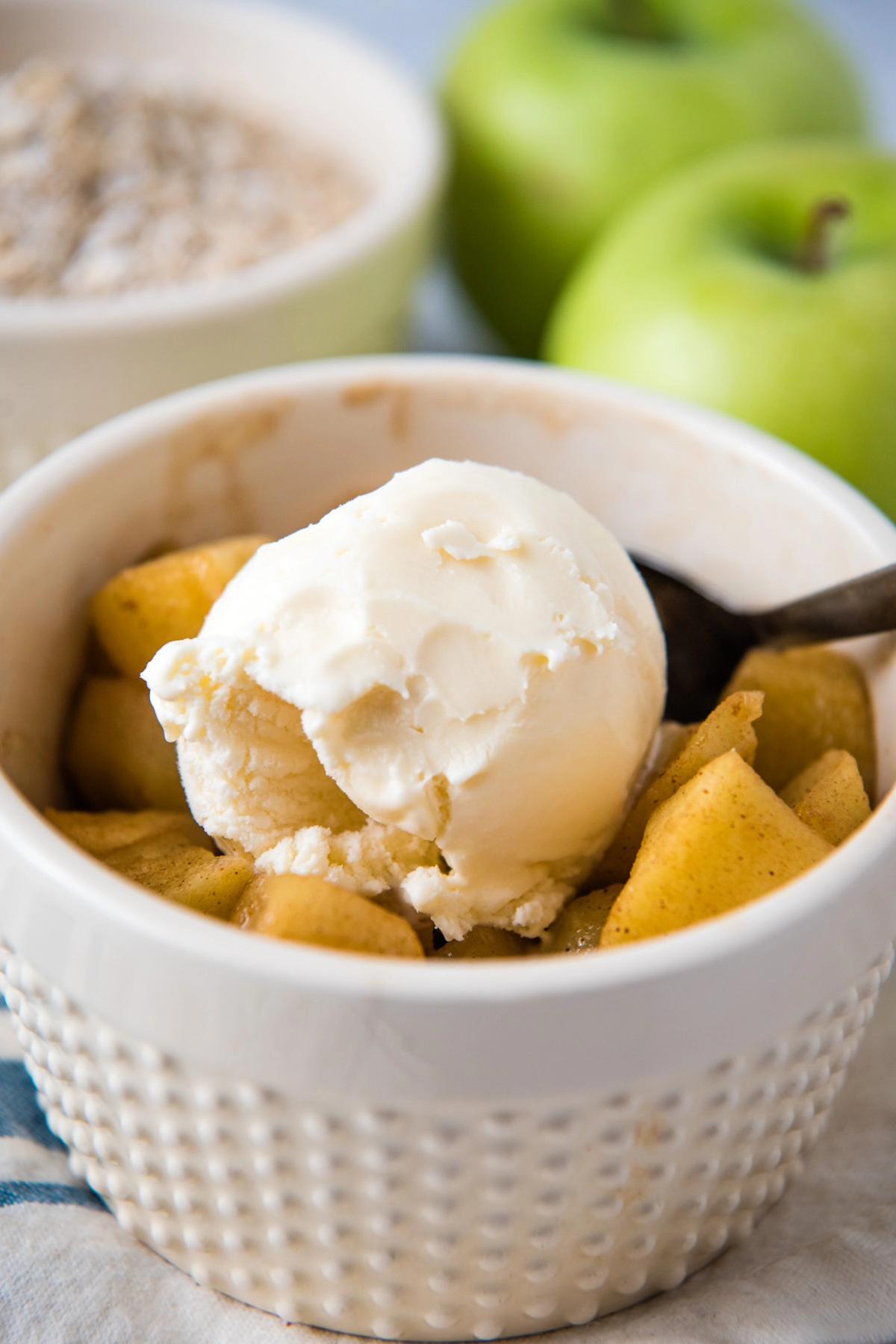 ivory ramekin full of microwave apples and cinnamon, topped with scoop of vanilla ice cream