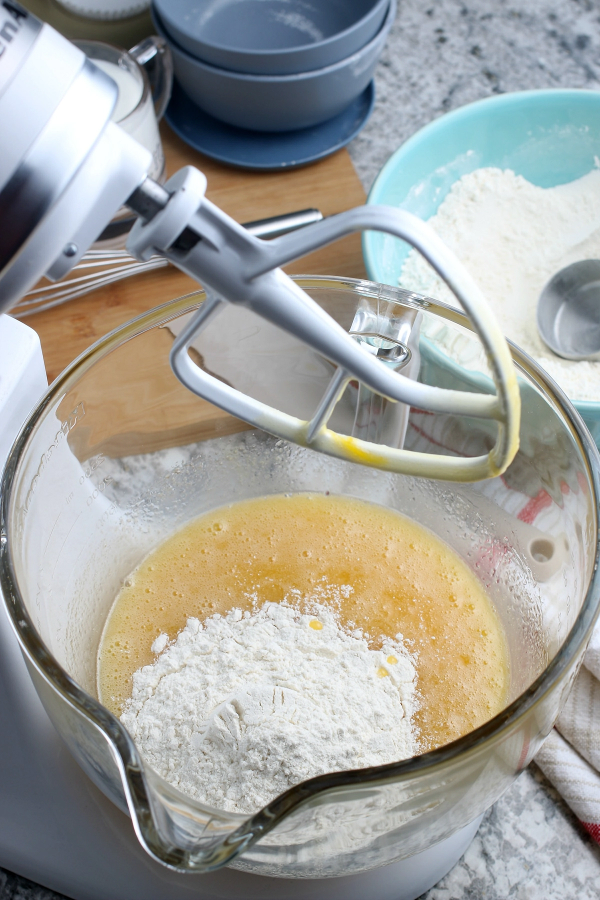 adding gluten-free dry ingredients to vanilla cupcake batter in glass mixing bowl on stand mixer