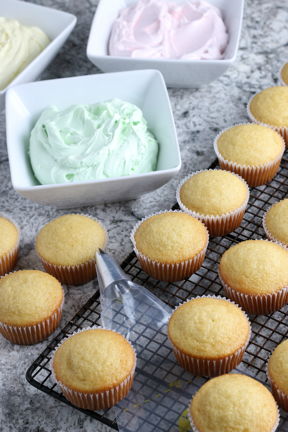 baked vanilla gluten-free cupcakes with green buttercream frosting and pastry bag on wire rack