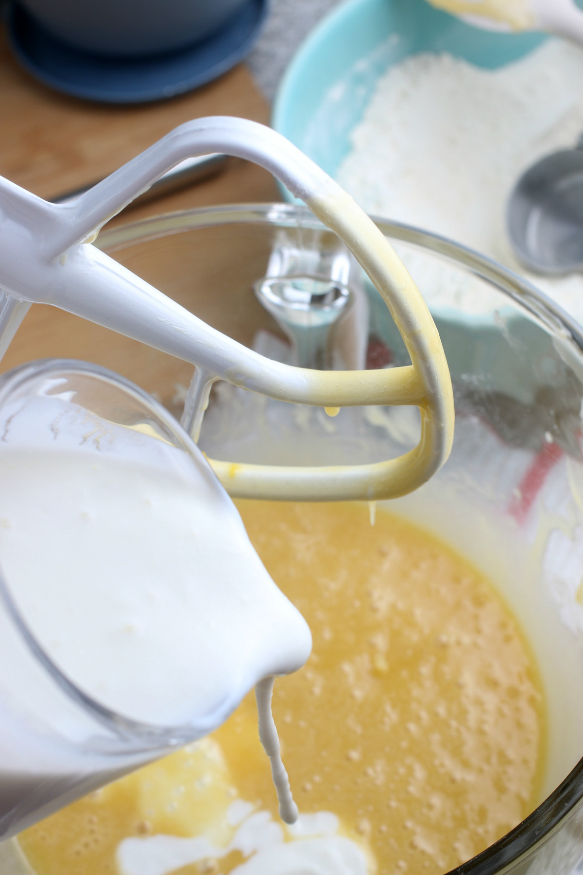 pouring buttermilk into gluten-free vanilla cupcake batter in glass bowl on stand mixer