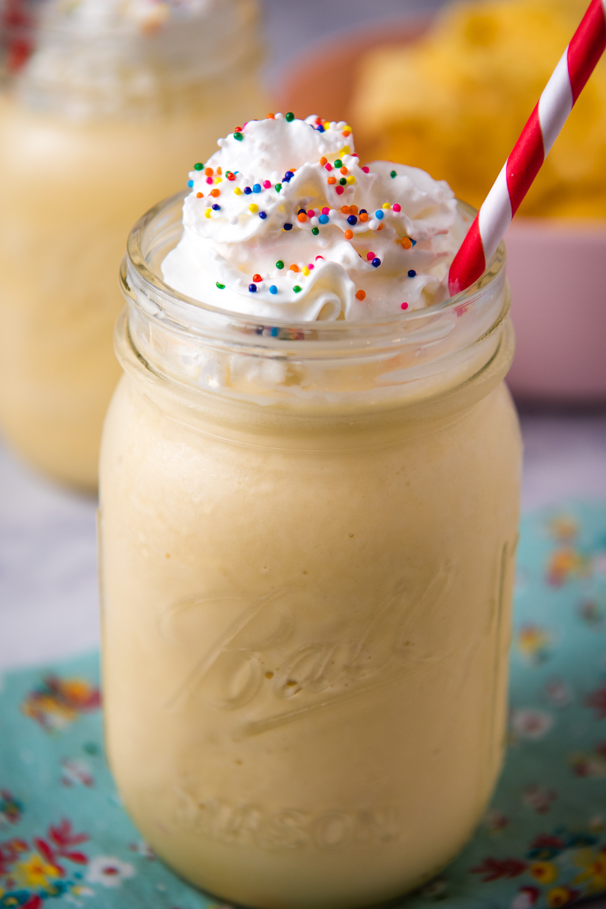 homemade vanilla milkshake, topped with whipped cream and sprinkles, in mason jar with straw