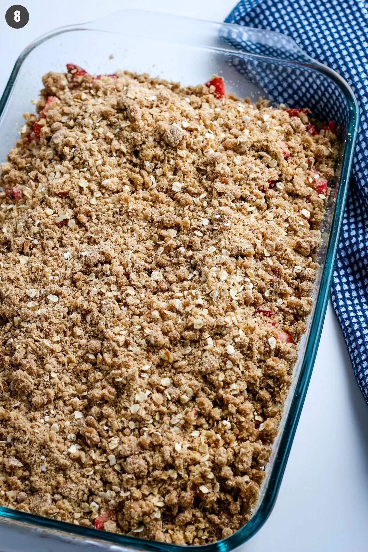crumbled topping over gluten free rhubarb strawberry crisp in glass baking dish