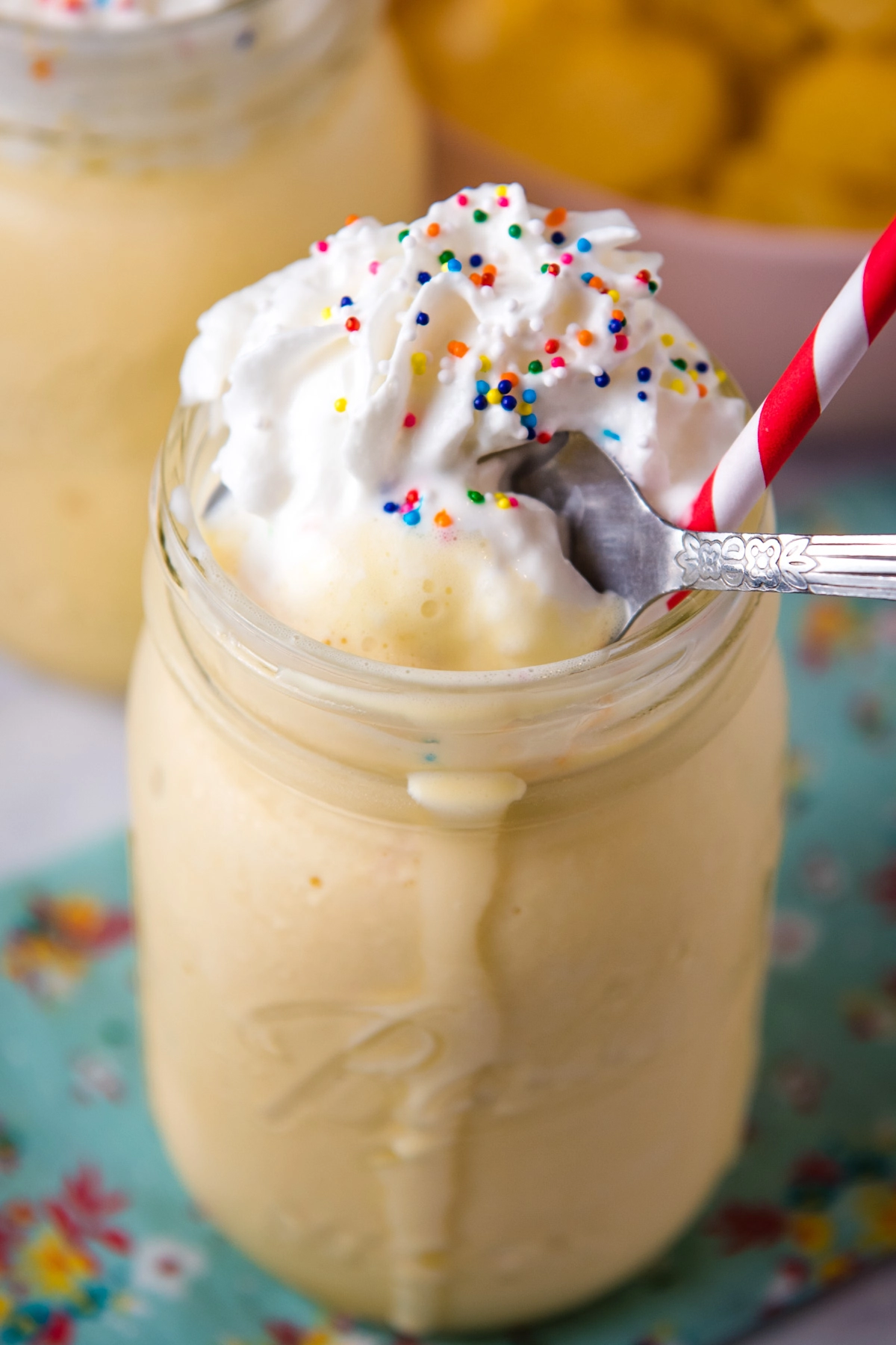 spoonful of vanilla shake, topped with whipped cream and sprinkles, in mason jar with straw