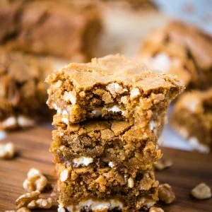 stack of gluten-free blondies on small wooden cutting board with walnuts all around