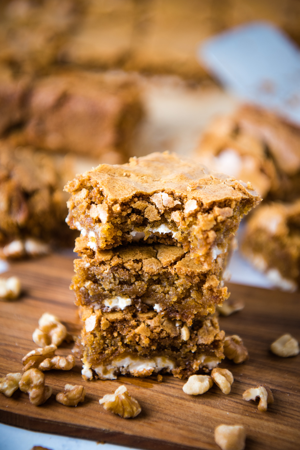 stack of gluten-free blondies on small wooden cutting board with walnuts all around