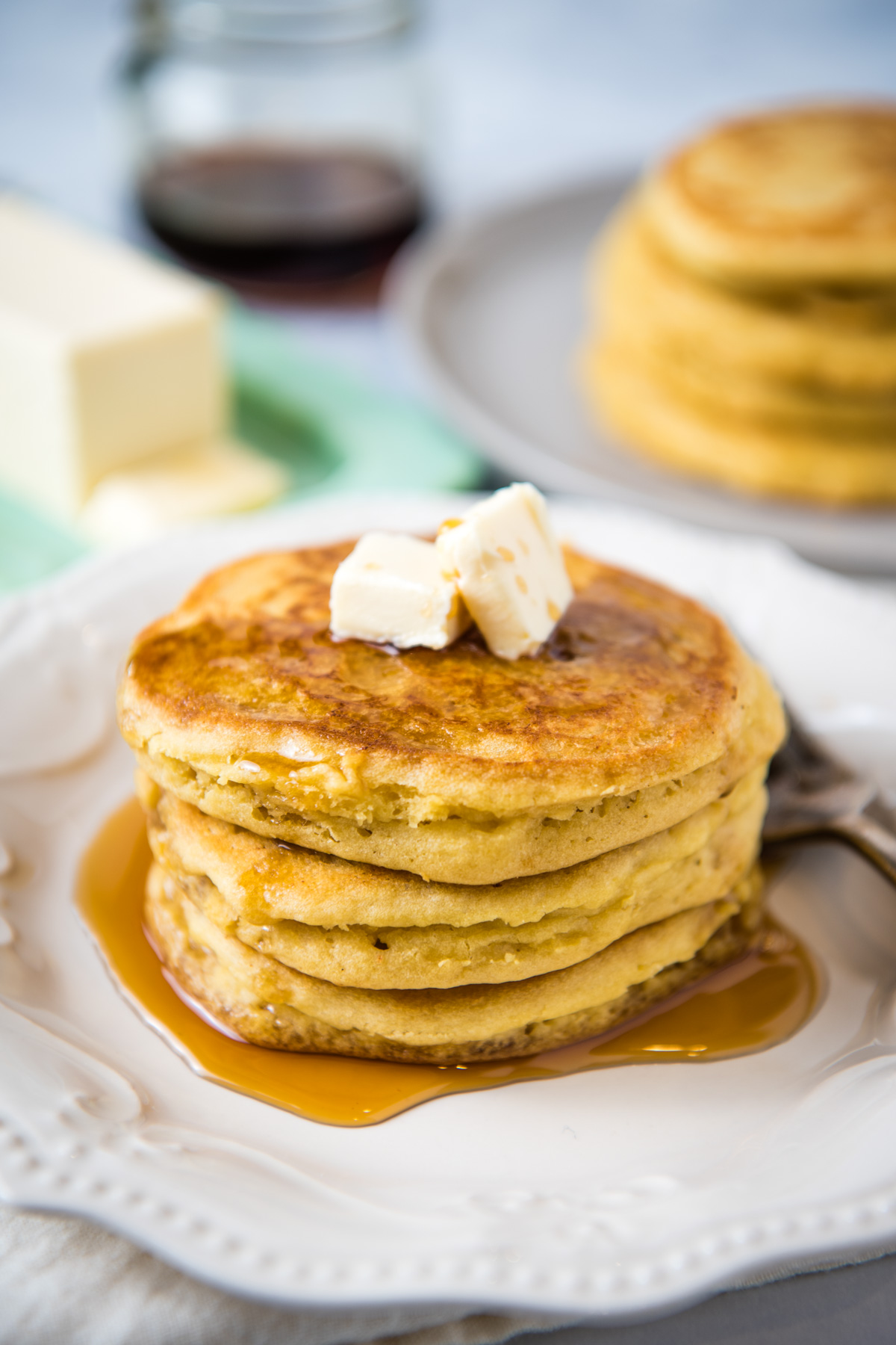 stack of gluten-free American pancakes with butter and maple syrup on white plate with fork