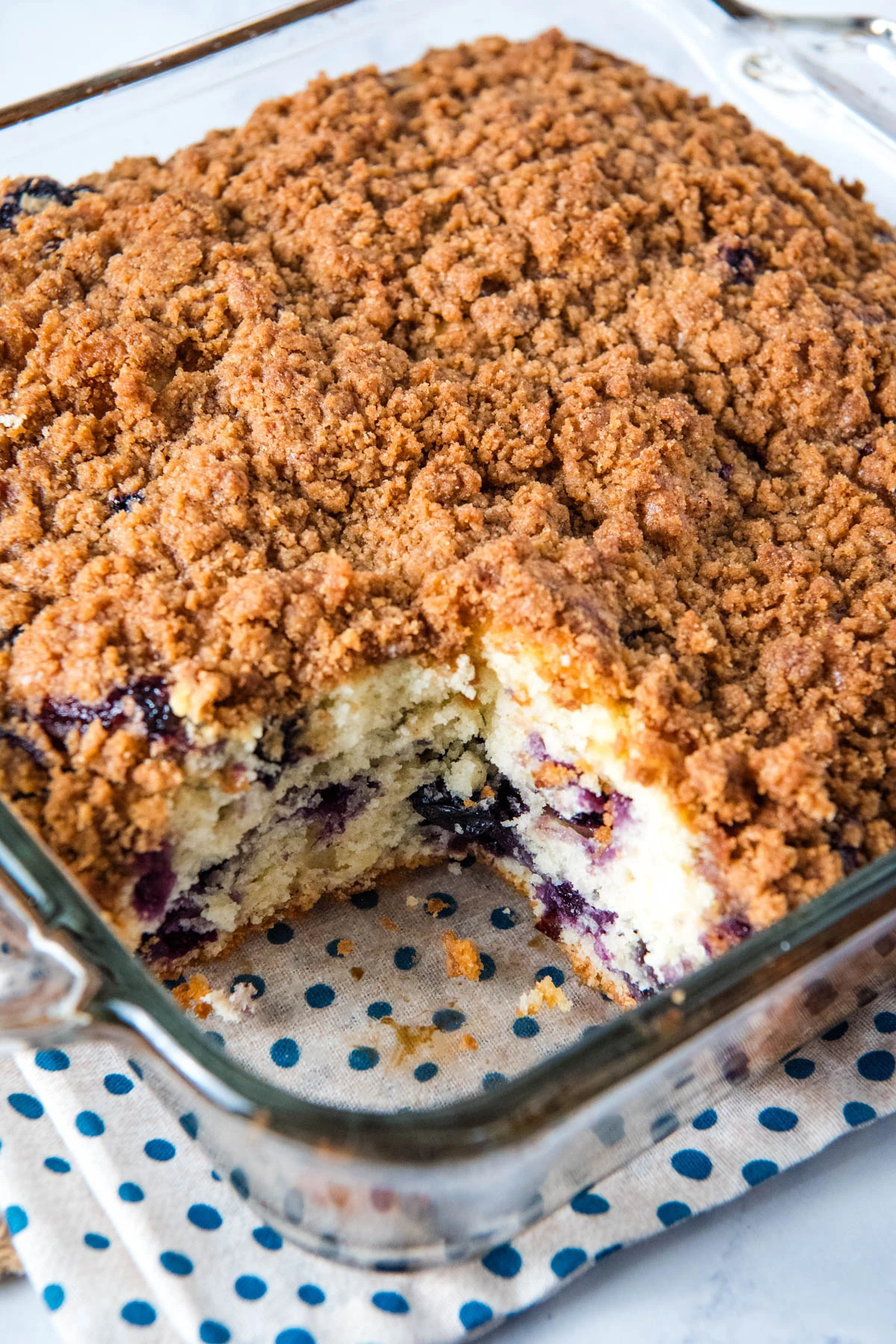 blueberry crumb cake with a sliced square cut out in a large glass baking dish on a white and blue polka dot decorative towel