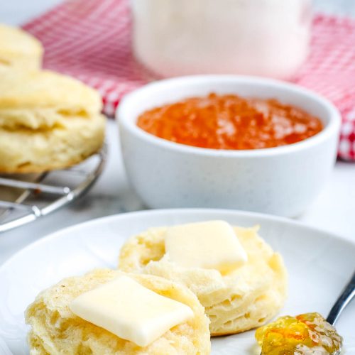homemade biscuits from biscuit mix cut in half and lathered in butter on a small white plate next to a spoonful of jelly