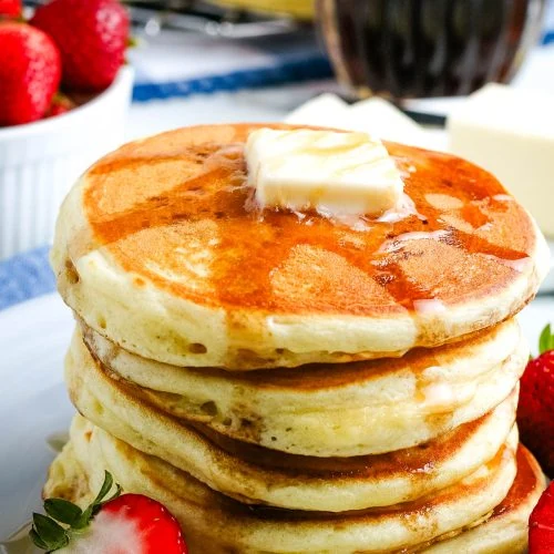 tall stack of homemade pancakes lathered in maple syrup on a small gray plate with fresh strawberries