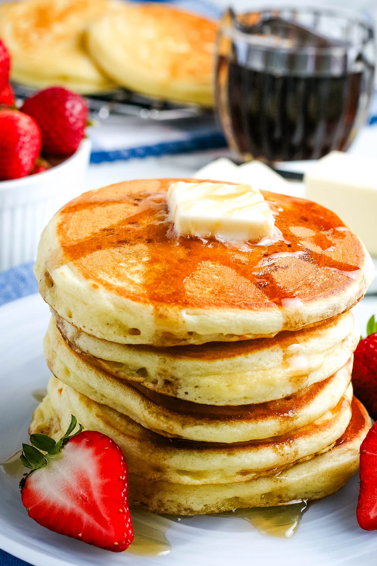 tall stack of homemade pancakes lathered in maple syrup on a small gray plate with fresh strawberries