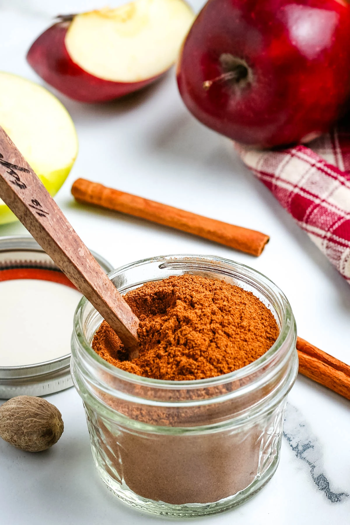 DIY apple pie spice in a small glass jar with a small wooden serving spoon