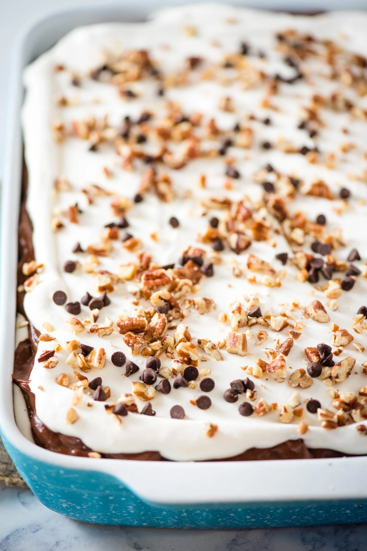 chocolate delight topped off with mini chocolate chips and chopped pecans in a large blue and white baking dish
