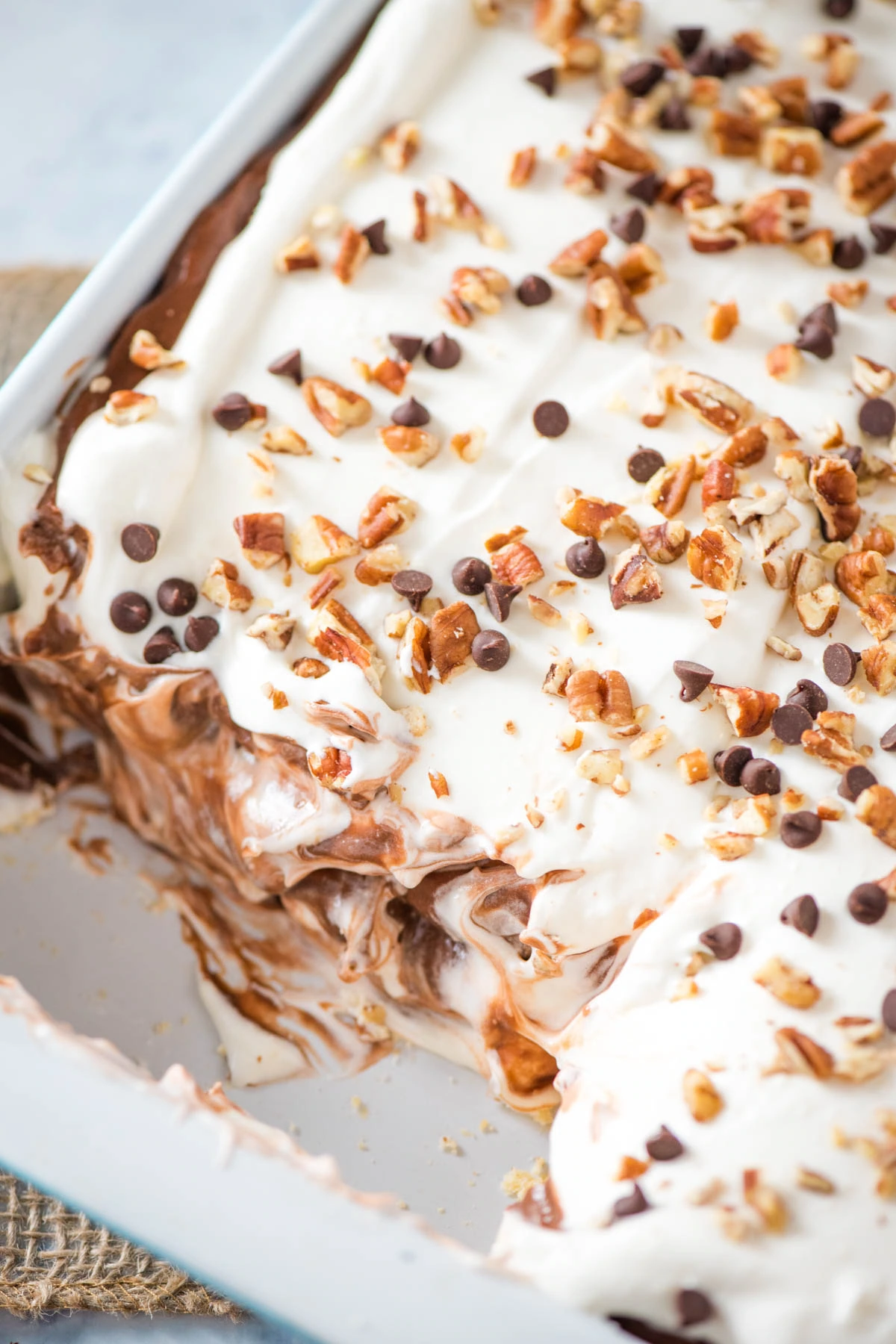 no bake chocolate delight recipe in a large blue and white baking dish with mini chocolate chips and chopped pecans on top