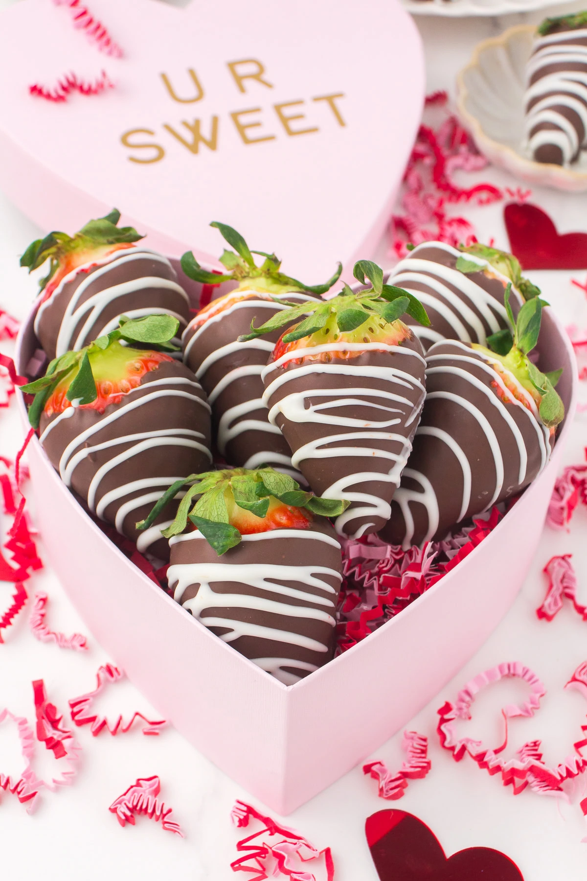 pink heart shaped box full of chocolate dipped strawberries with a white chocolate drizzle