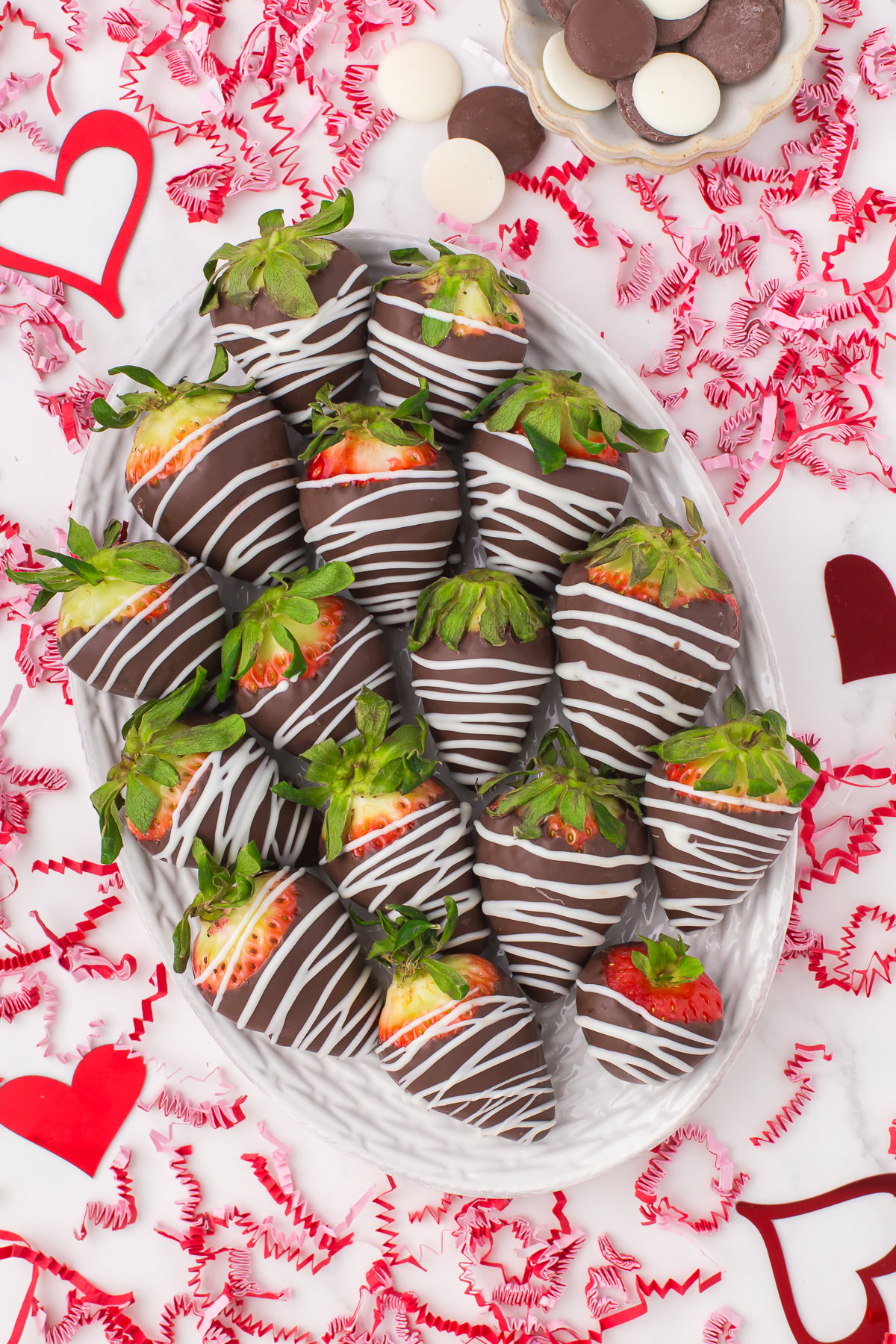 large decorative plate full of chocolate homemade chocolate covered strawberries with Valentine's Day confetti all around on the countertop for decoration
