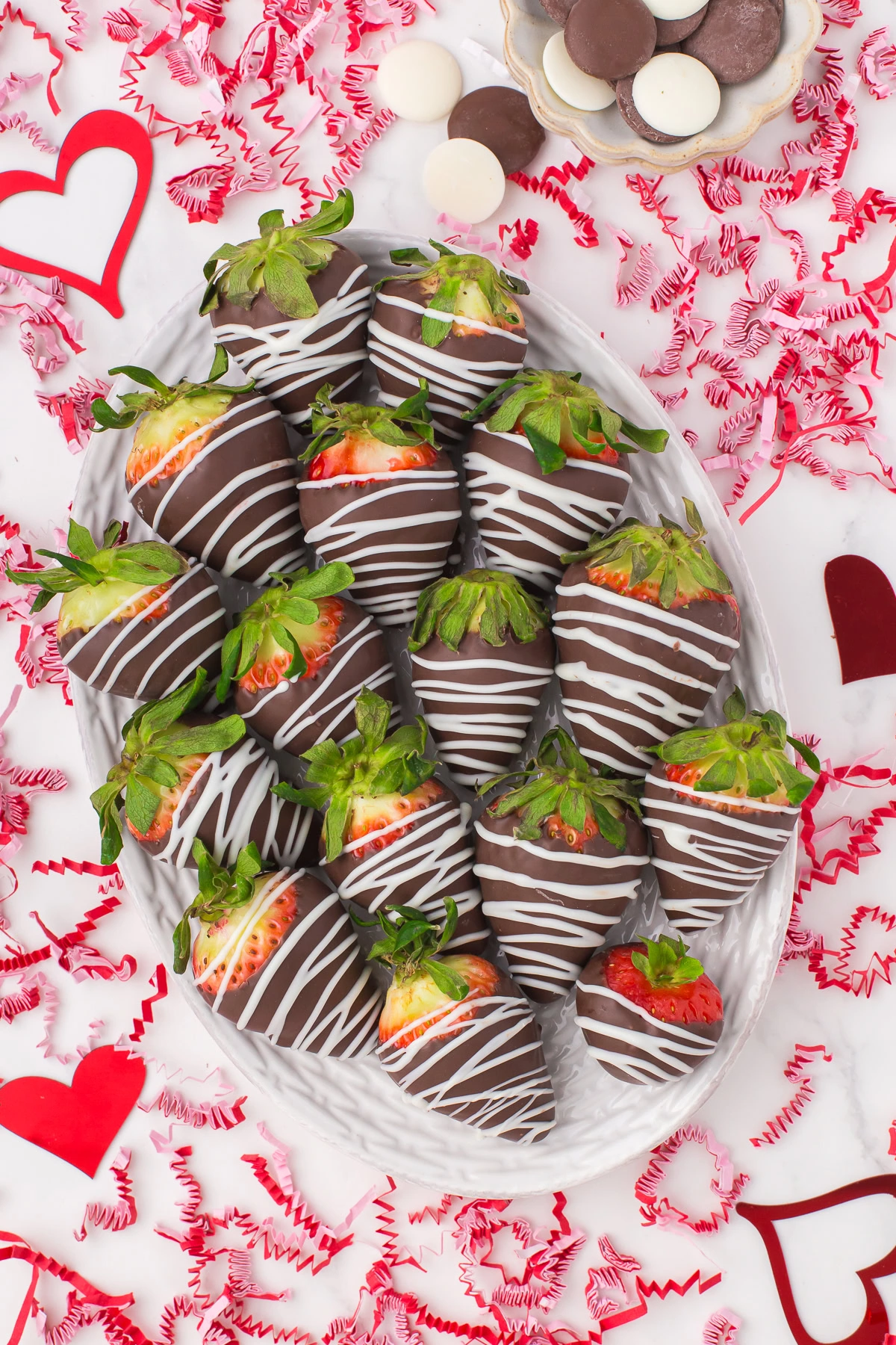 large decorative plate full of chocolate homemade chocolate covered strawberries with Valentine's Day confetti all around on the countertop for decoration
