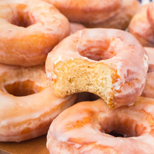 classic glazed donuts stacked up on a decorative wooden cutting board with a bite taken out