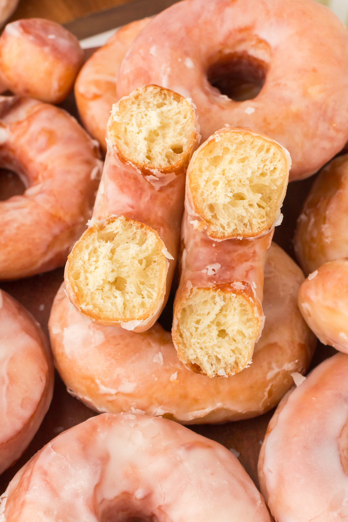 homemade glazed donuts piled up with one on top torn in half