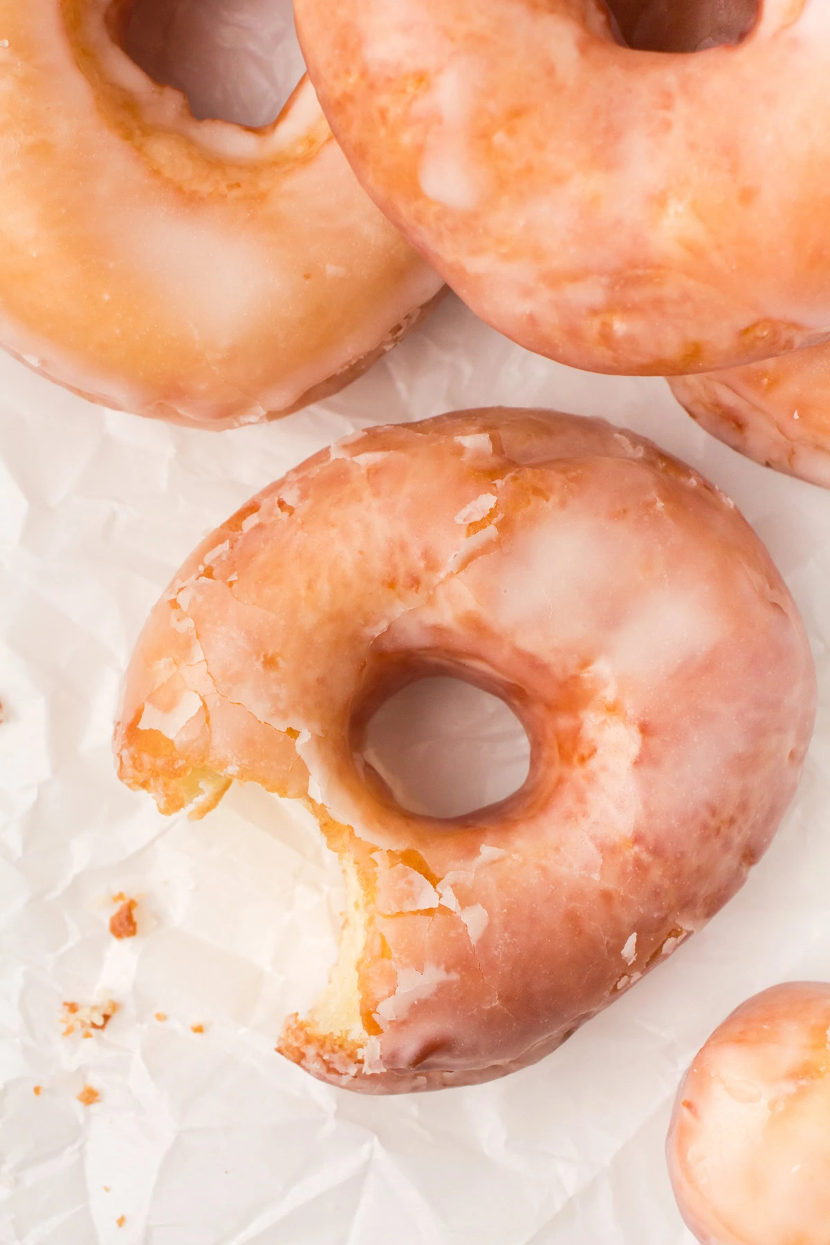 overhead shot showing homemade glazed donuts on a white countertop with a bite taken out