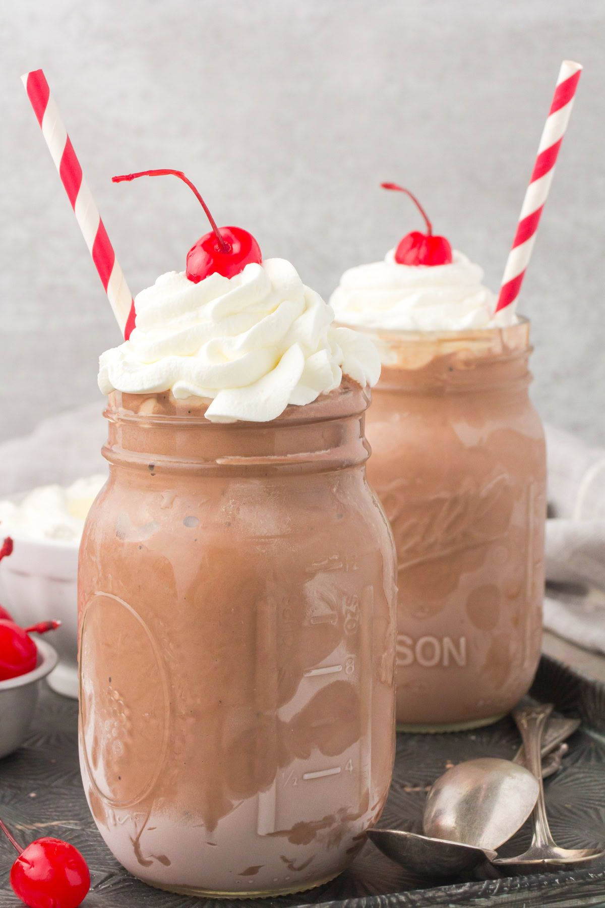 homemade chocolate milkshakes in small glass mason jars with whipped cream and a cherry on top