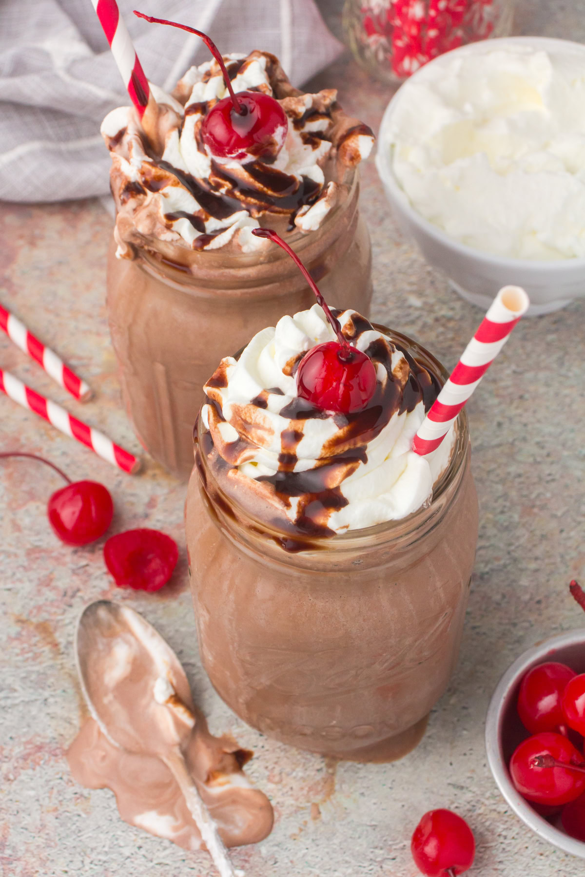 easy chocolate milkshakes in small glass mason jars with whipped cream, a chocolate syrup drizzle, and a cherry on top