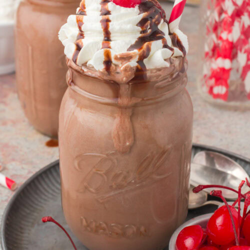 homemade chocolate milkshake with whipped cream, a chocolate syrup drizzle, and cherries on top with a red and white candy cane-striped straw