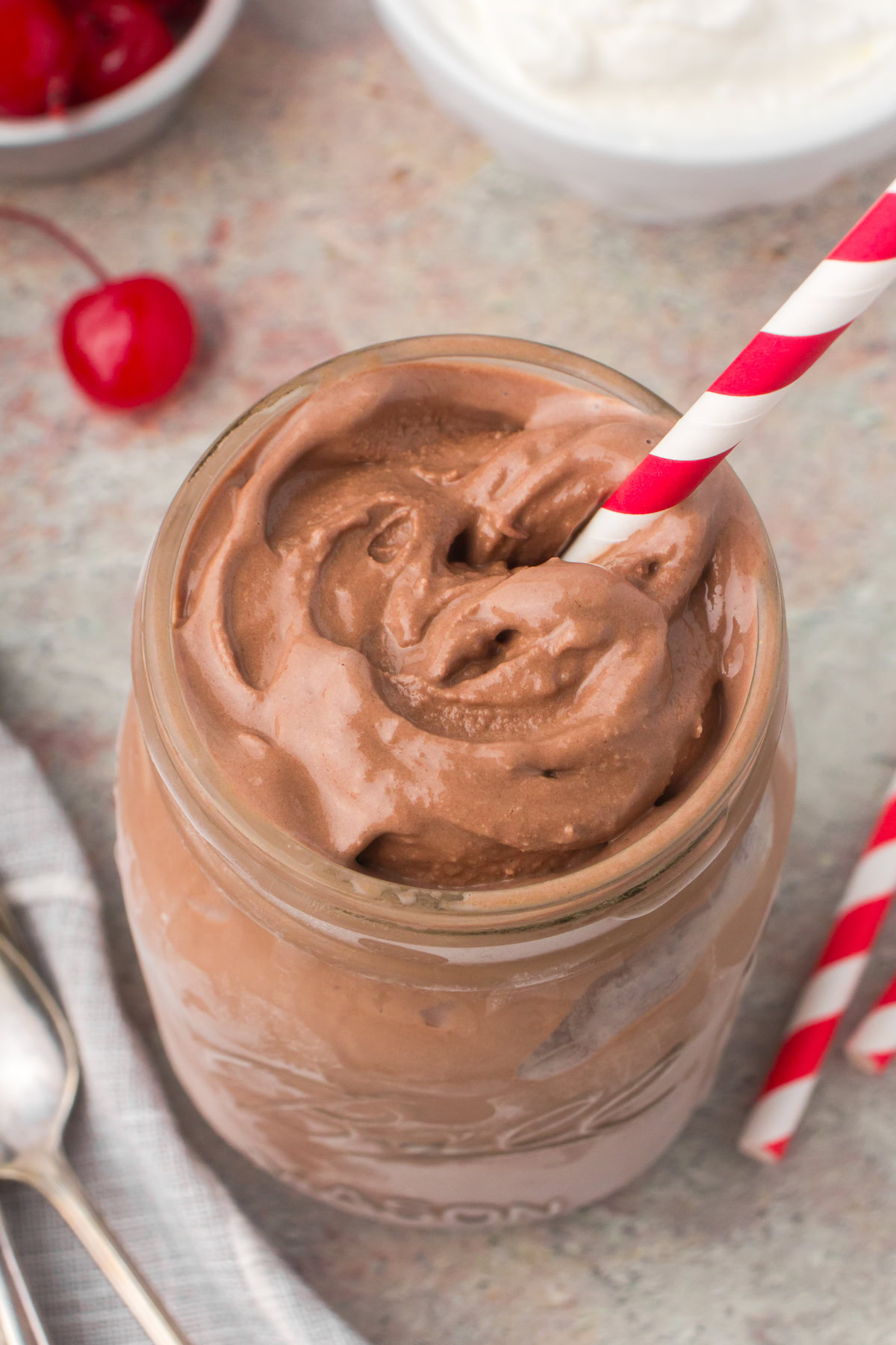 thick and creamy chocolate milkshake in a small glass mason jar with a red and white candy cane-striped straw stuck inside