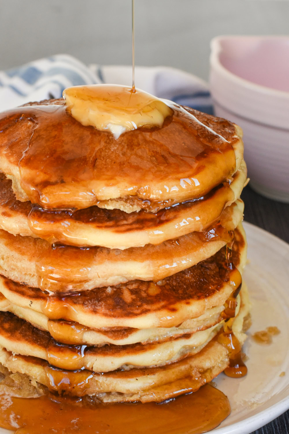 towering stack of homemade pancakes from scratch lathered in butter and drizzled in maple syrup on a gray plate