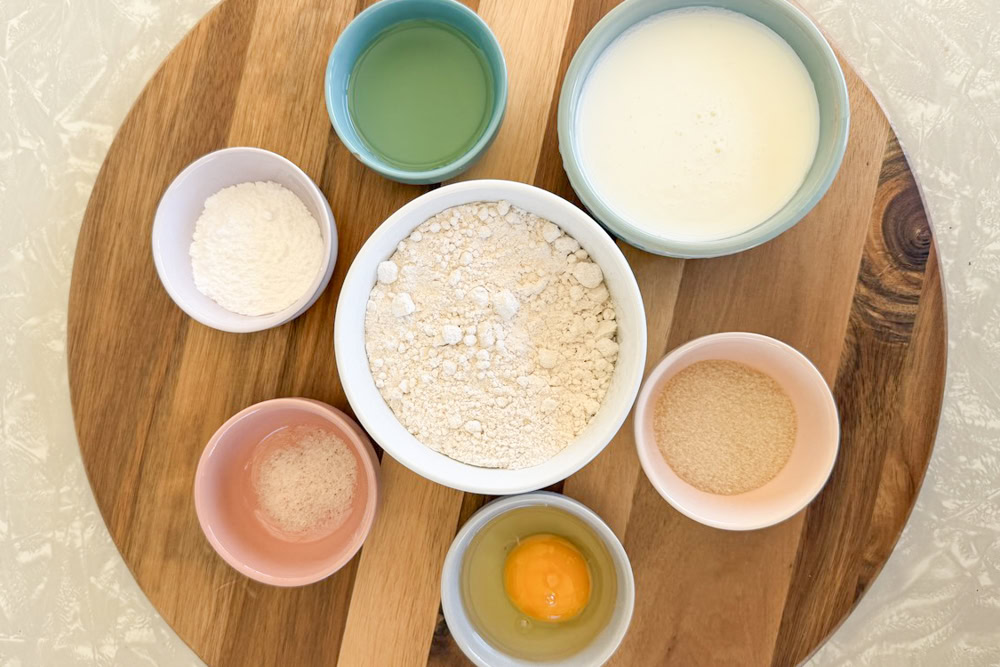overhead shot showing homemade pancakes ingredients set out separately in little colored bowls on a circular wooden cutting board